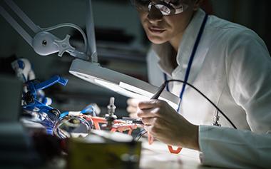 A women, in a lab coat, at a work table.